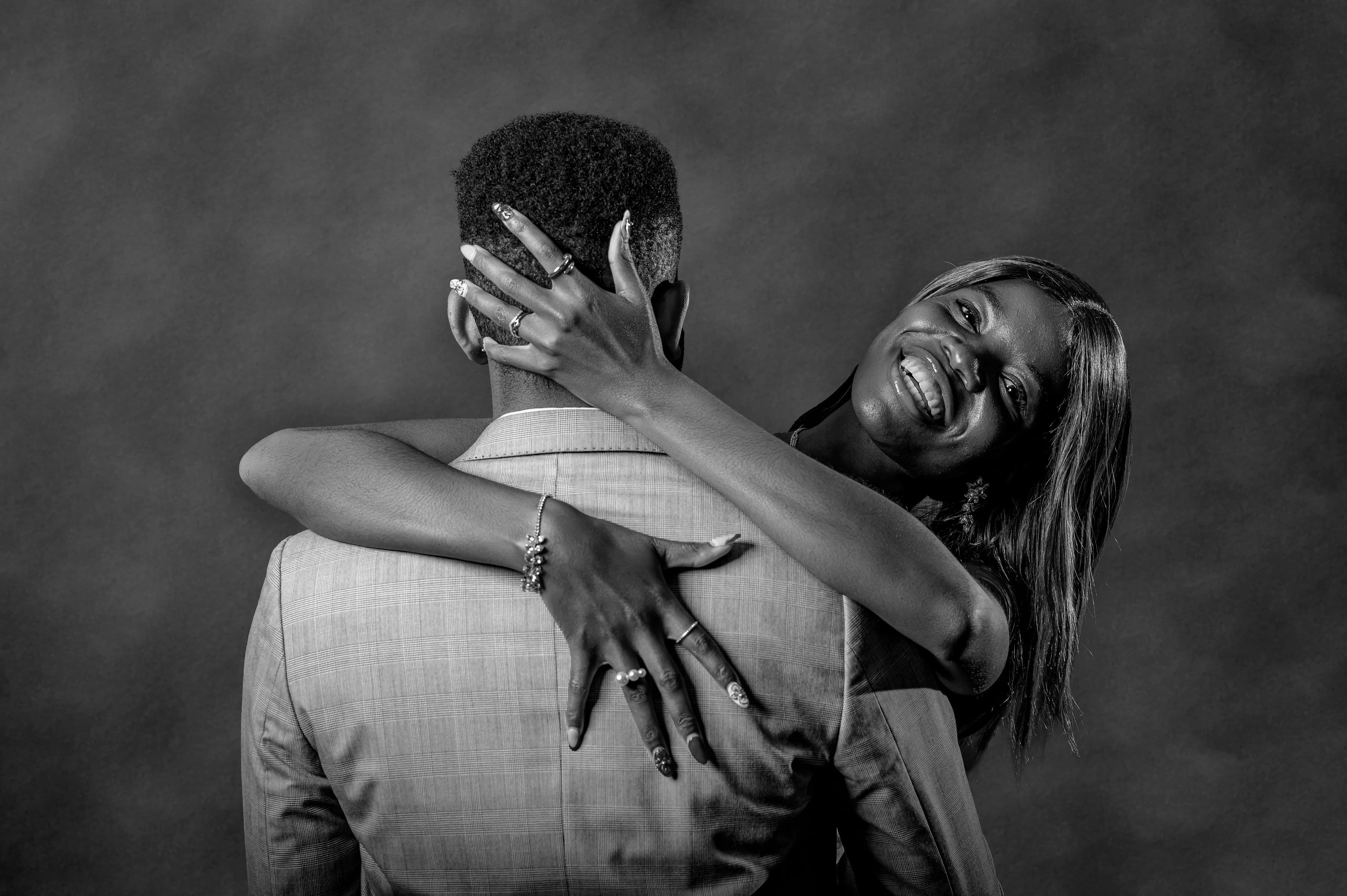 Black and white photo of Esther embracing David from behind, beaming over his shoulder
