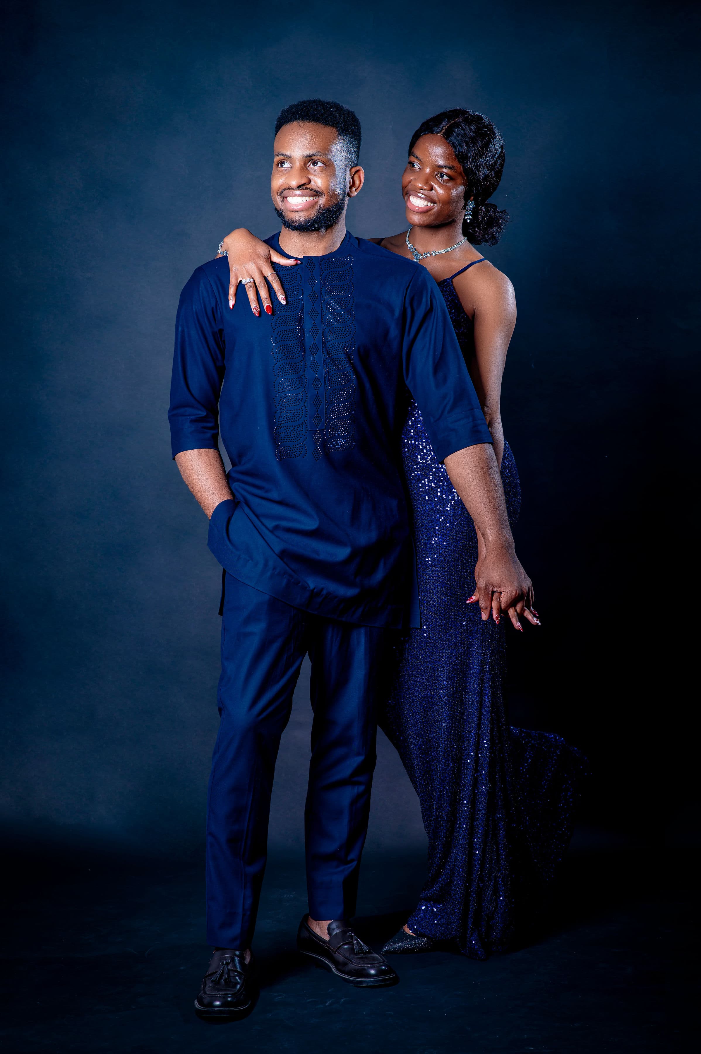 David in navy native wear and Esther in a sequinned gown, looking away together